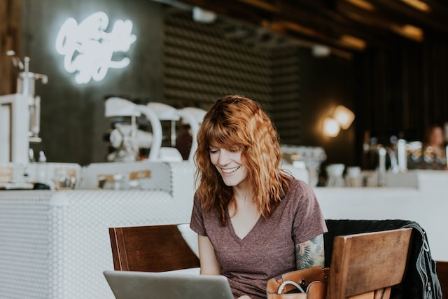 A woman sits at a table with her laptop at a coffee shop. 