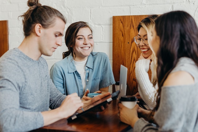 A group of coworkers come together around a wood table with an iPad.