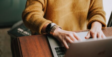 A person in an orange sweater works on a laptop.