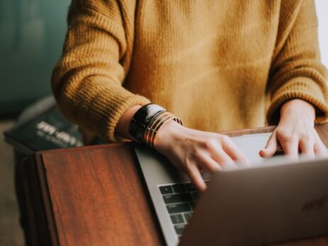 A person in an orange sweater works on a laptop.