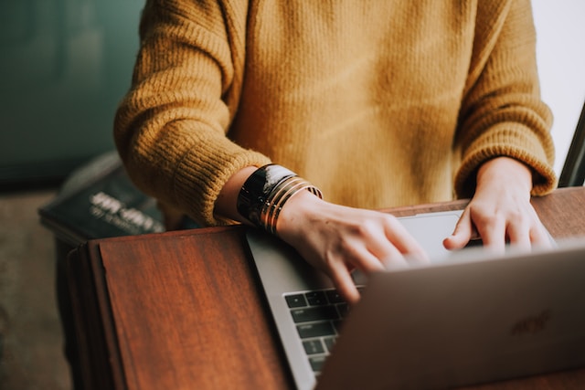 A person in an orange sweater works on a laptop.