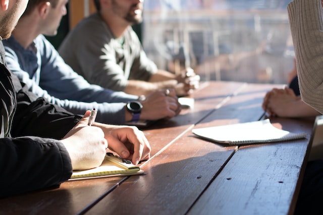 People sit at a table in front of a man with a pad of paper.