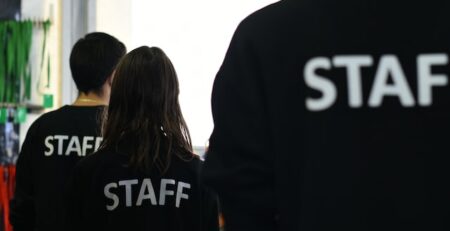 Three people in black shirts with Staff printed across the back. 