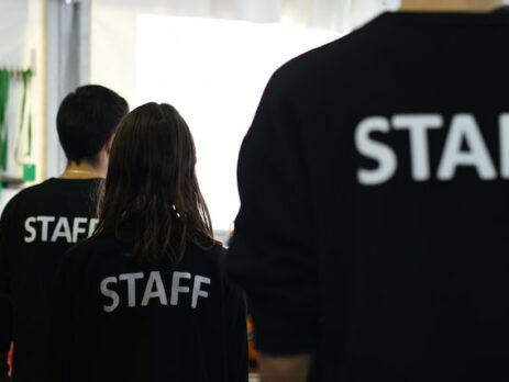 Three people in black shirts with Staff printed across the back. 