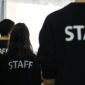 Three people in black shirts with Staff printed across the back. 