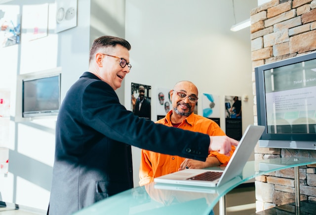 A manager in a suit points something out to an employee on a computer.