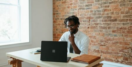 A man works at a laptop at his desk in an office. 