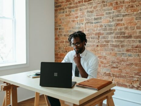 A man works at a laptop at his desk in an office. 