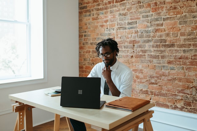 A man works at a laptop at his desk in an office. 