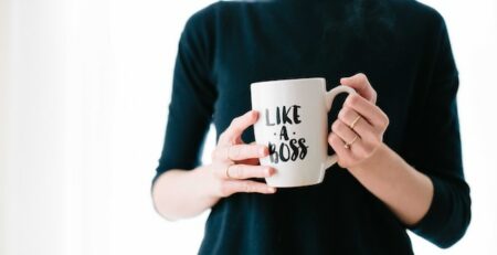 A woman in a green sweater holds a mug that says “like a boss.”