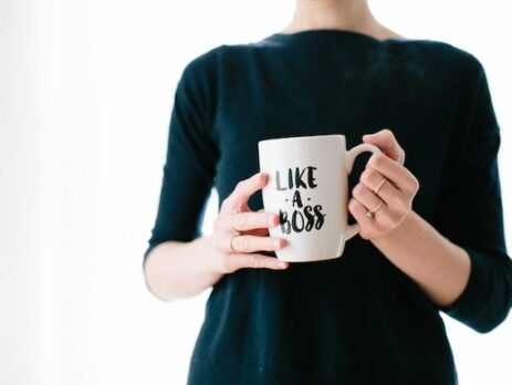 A woman in a green sweater holds a mug that says “like a boss.”