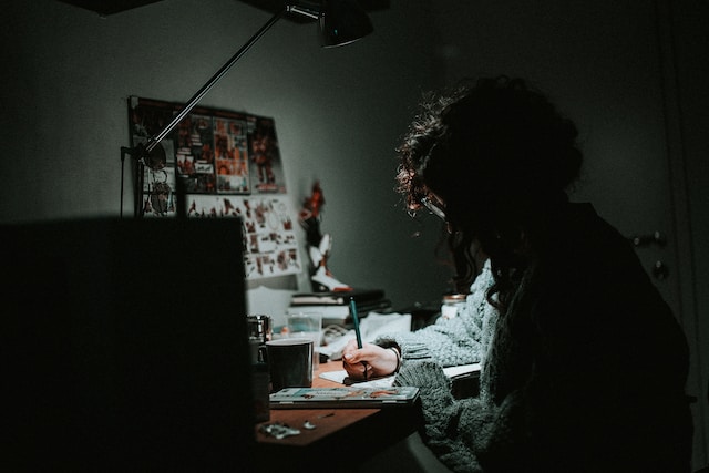A dark-haired woman works at a cluttered desk.