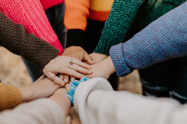 A group of people stand in a circle with one hand in the middle. 