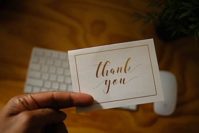 An individual holds a thank you note over a blurred out keyboard.
