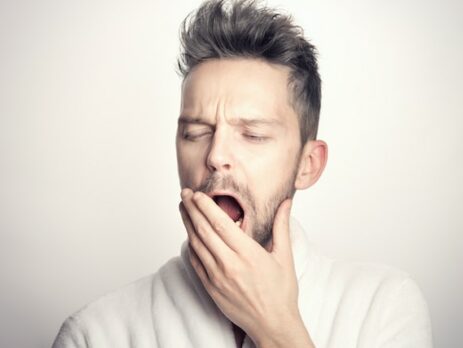 A man with light skin and dark hair yawns. 