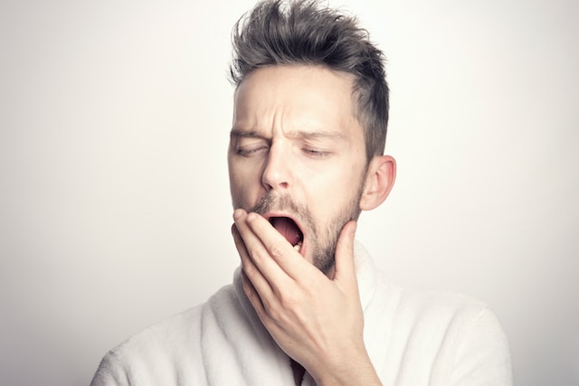 A man with light skin and dark hair yawns. 