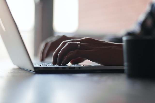 An individual types on a laptop that is placed on a desk.