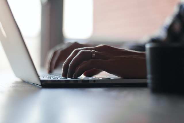 An individual types on a laptop that is placed on a desk. 