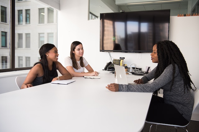 Three women sit around a table conducting an interview. 