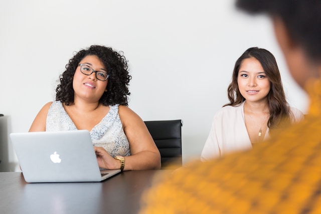 Two women sit across the table from a gentleman they are interviewing. One woman is using a laptop computer.