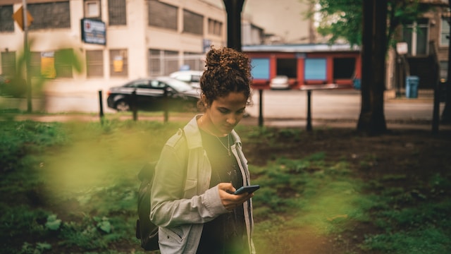 A Gen Zer looks at something on their smartphone while walking in the park.