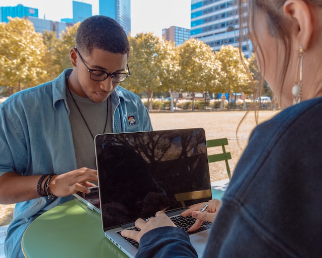 Two Gen Z students work on laptops in a park environment.