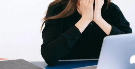 Stressed woman sitting at a desk and covering her face.