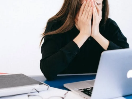 Stressed woman sitting at a desk and covering her face.