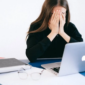 Stressed woman sitting at a desk and covering her face.