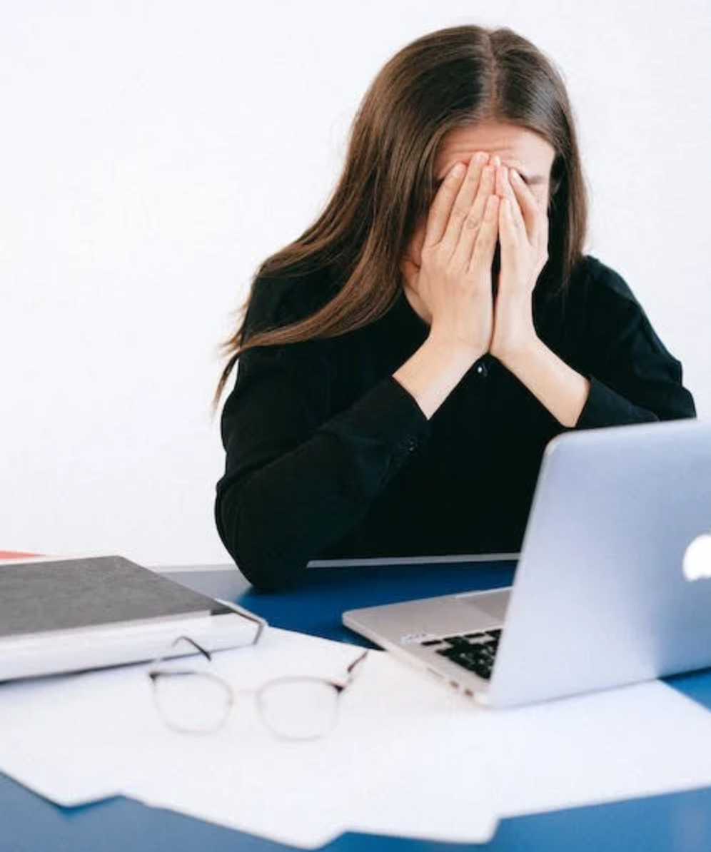 Stressed woman sitting at a desk and covering her face.