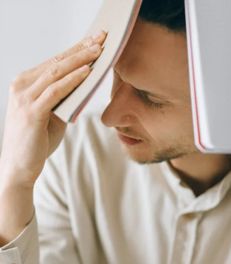 An anxious employee sitting at a desk and holding documents to his face.