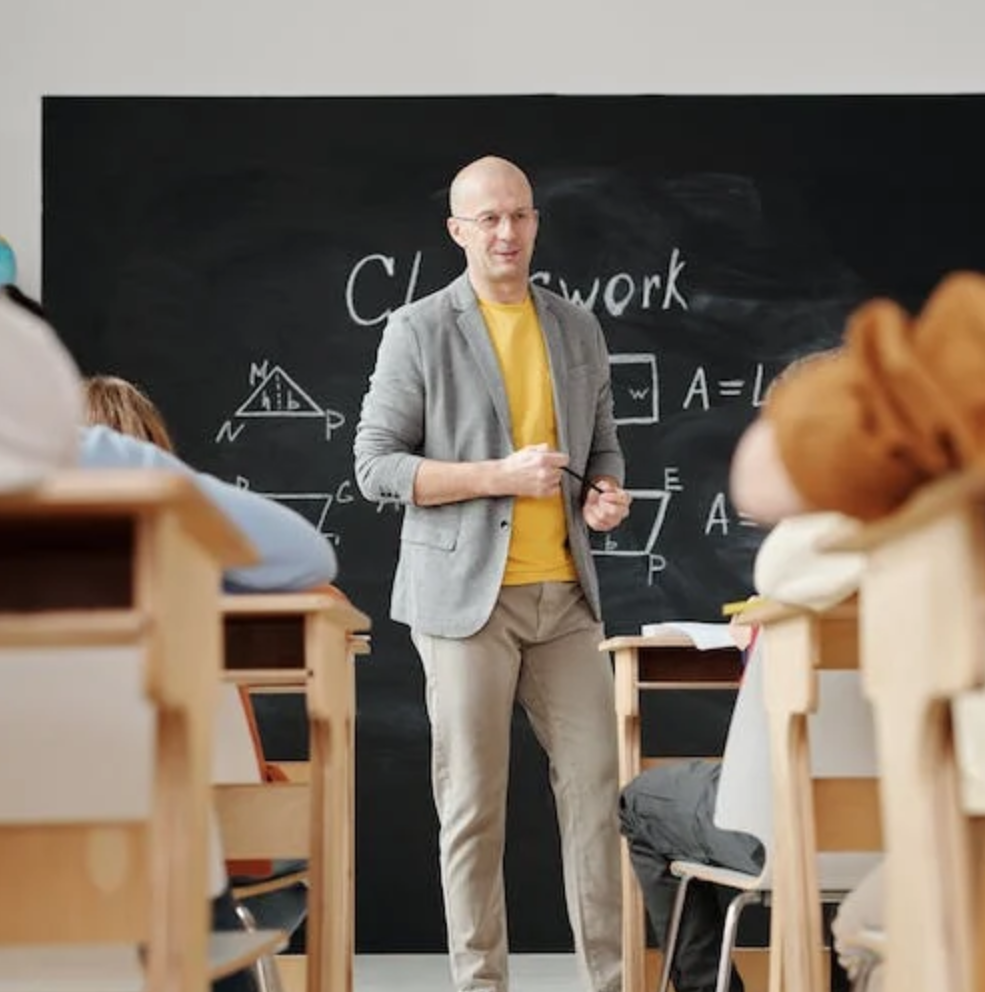 A teacher standing in front of a blackboard and facing students.