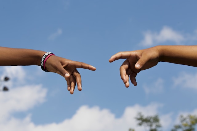 Two hands reach for each other in front of a blue sky background. 