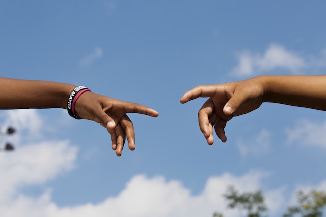 Two hands reach for each other in front of a blue sky background.