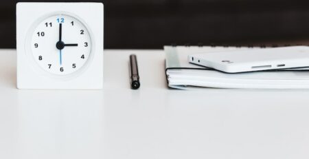 A clock placed on a table next to a pen and book