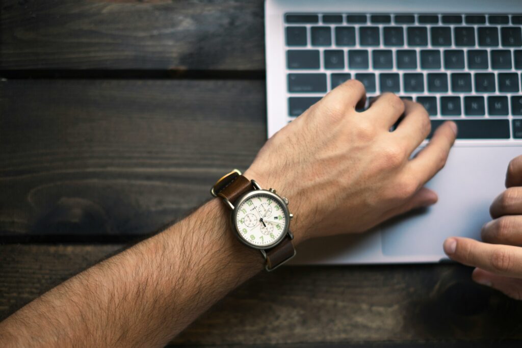 A man checking his watch with a laptop. 
