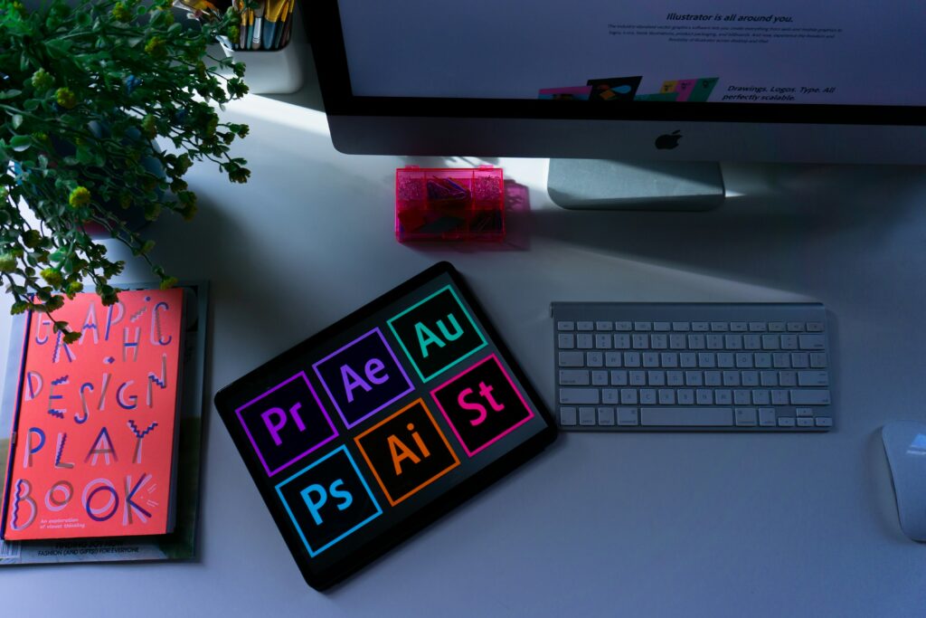 iPad shows the various Adobe software logos alongside a monitor and graphic design book.