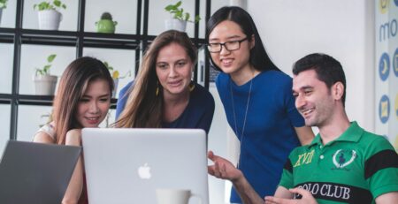 Four people watching on a white Macbook atop a glass table.