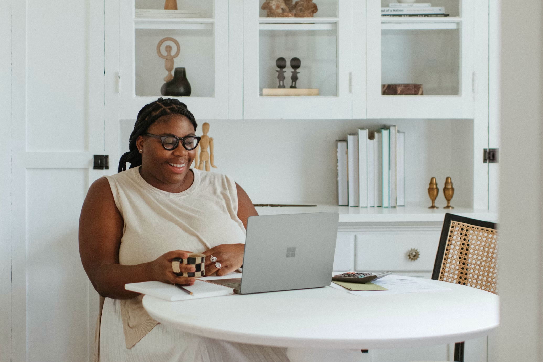 A woman smiles at her laptop while working at her kitchen table.