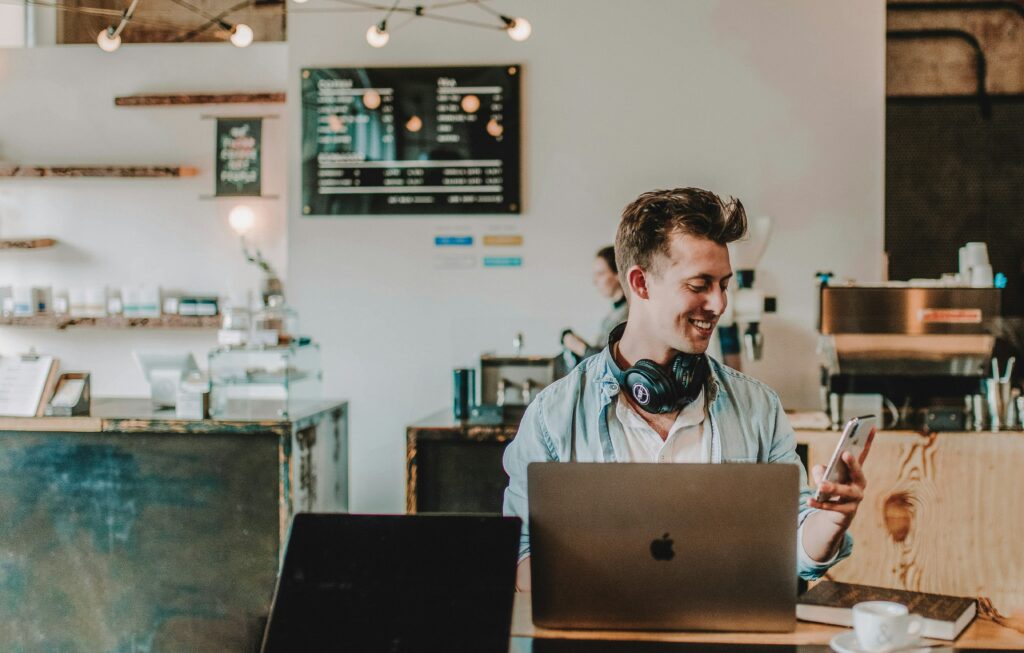 a guy in a coffee with headphones, phone and a laptop.